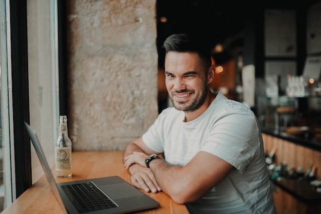 Blinking into the camera in a cafe in front of a computer laptop.
